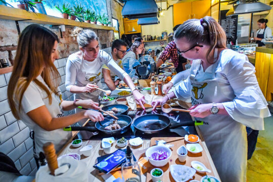 főzőiskola, nők kötényben főznek egy pultnál
