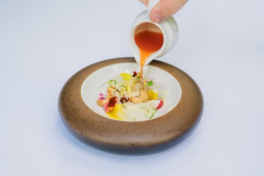 Michelin-csillag, barna-fehér tányérba kéz önt levest