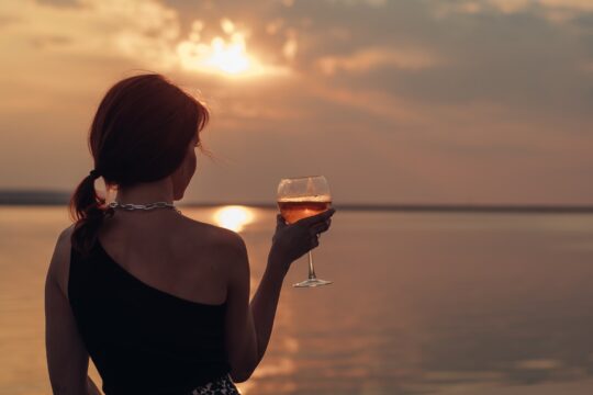 alkoholmentes bor, egy nő pohárral a kezében vízparton naplementét néz
