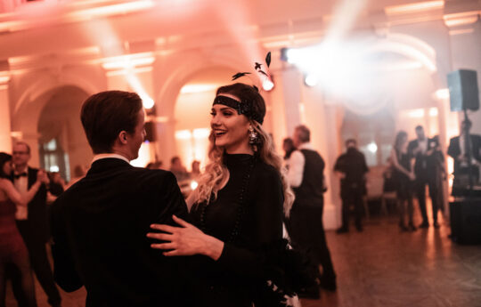 gatsby, fekete ruhás nő és férfi táncol egy teremben
