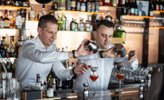 két férfi áll egy bárpult mögött, folyadékot öntenek pohárba