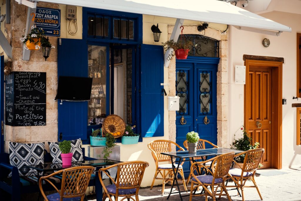 fehér épület kék ajtóval Kréta szigetén, előtte asztalok