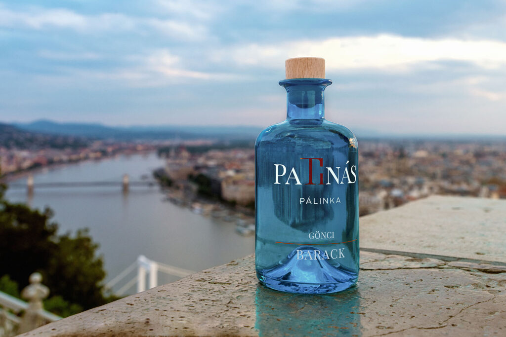 kék patinás pálinka üveg, mögötte a háttérben egy város