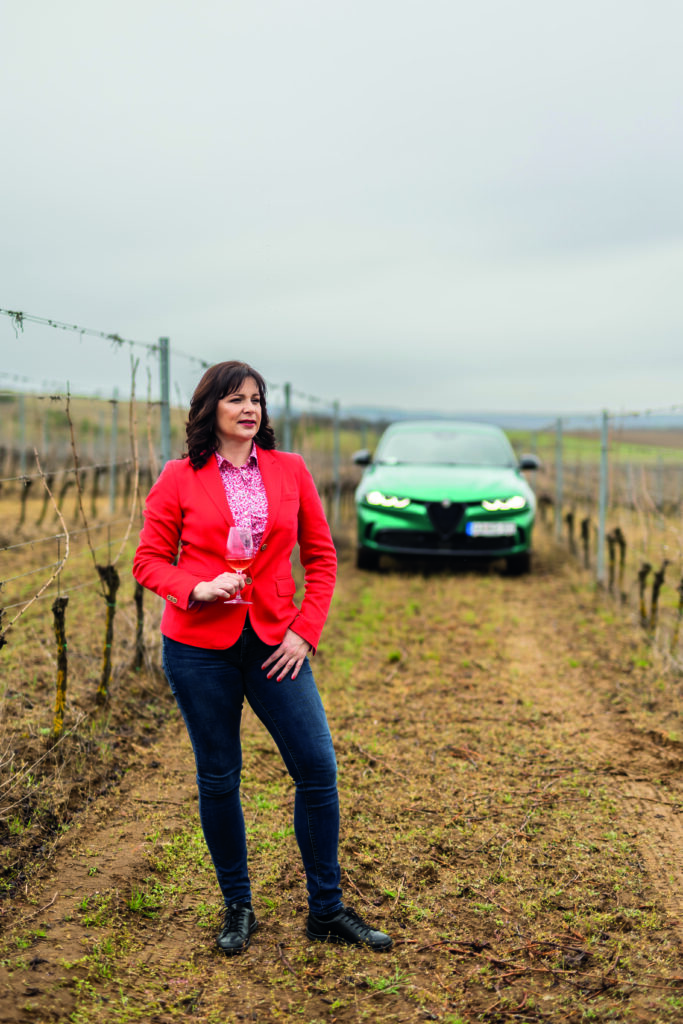 egy nő áll a szőlőben háttérben zöld autó
