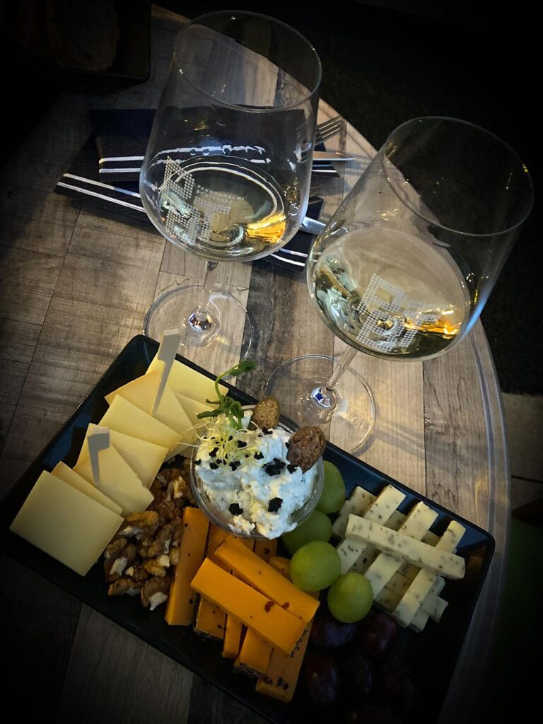 sárga sajtok egy tálon, mellette átlátszó talpas poharak