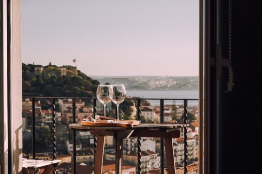 két pohár bor az asztalon, háttérben kilátás Lisszabonra