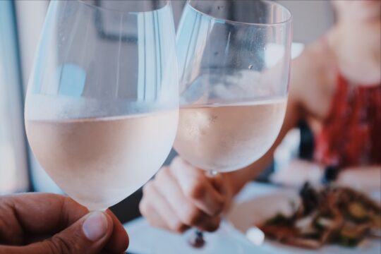 két kéz rosé borral a pohárban koccint
