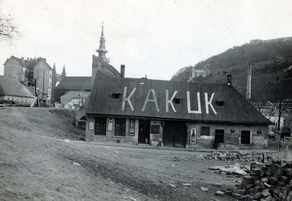 fekete-fehér képen egyszintes épület, tetején felirat, tabán