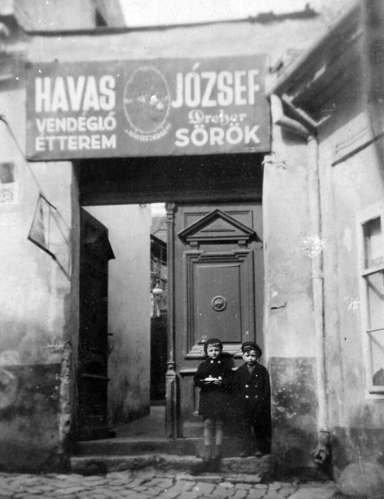 fekete-fehér képen két gyerek áll egy kapuban, fölöttük felirat, tabán