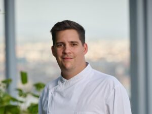 férfi fehér kabátban, mögötte nagy ablak