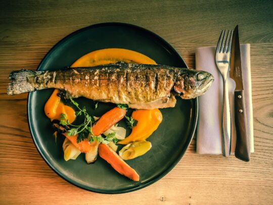 sült hal sötét tányéron, körülötte zöldség