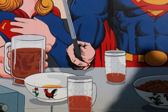 superman asztalnál ül, előtte korsó sör