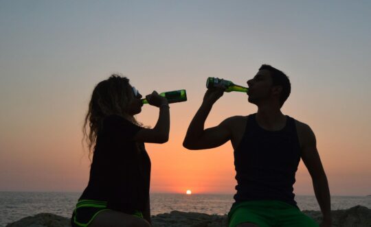 egy nő és egy férfi naplementében, kezükben sör