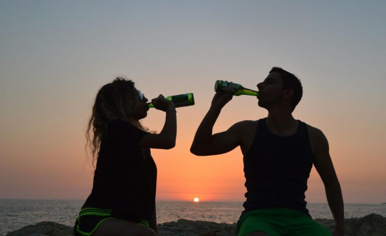 egy nő és egy férfi naplementében, kezükben sör