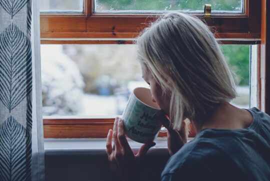 egy nő csészéből iszik egy ablaknál