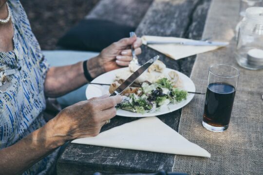 fehér tányéron saláta, egy idős ember késsel-villával eszik