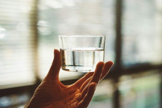 átlátszó pohár egy kézben, a pohárban átlátszó folyadék