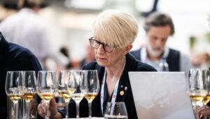 szemüveges nő ül asztalnál, előtte borospoharak