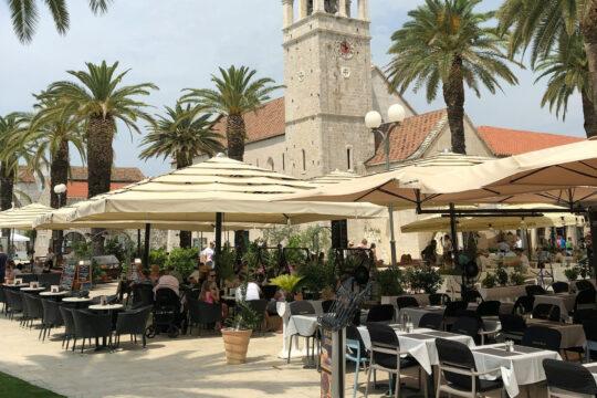 étterem terasza ernyőkkel, székekkel, asztalokkal, háttérben templom, Horvátország, Split